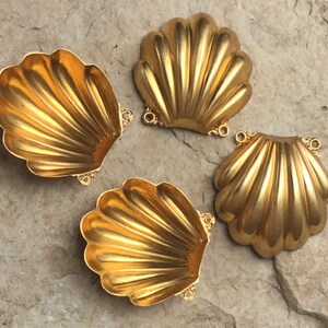 May include: Four gold-colored metal seashell-shaped ornaments with decorative details. Each seashell has a slightly different shape and size.