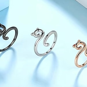 May include: Three cat-shaped rings in different colors: black, silver, and gold. The rings are made of metal and have a simple design.