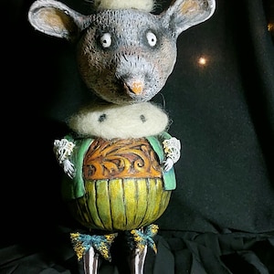 Pode incluir: Uma figurinha de rato feita à mão e caprichosa que usa uma coroa dourada, uma jaqueta verde e calças amarelas. O rato tem um colar de pele branca e está em pé sobre uma superfície preta.