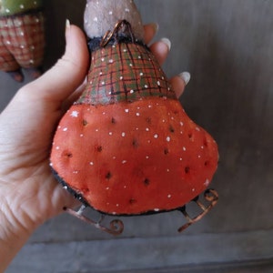 May include: A handmade felt bunny wearing a plaid and red dress with white polka dots. The bunny is on a pair of metal skis with a wire loop for hanging.