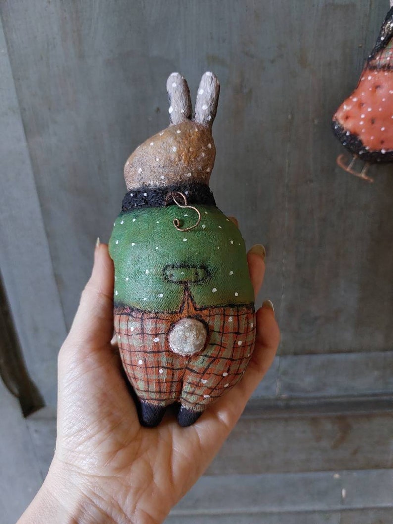 May include: A handmade plush bunny toy wearing a green and white polka dot shirt and red and white checked trousers. The bunny has a white fluffy tail and brown painted eyes.
