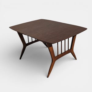 May include: A mid-century modern coffee table with a dark brown, rectangular top and angled legs. The table has a wooden frame with a slatted design on the sides, and measures approximately 30 inches long and 20 inches wide.