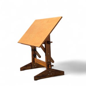 May include: A vintage wooden drafting table with an adjustable, light-colored top. The table has a dark brown, sturdy base and frame with adjustable knobs and hinges. The angled tabletop is supported by a wooden frame.