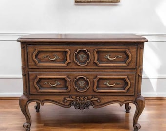 May include: A two-drawer wooden chest with ornate carvings and brass hardware. The chest has a dark brown finish and sits on four cabriole legs.