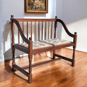 May include: A wooden bench with a curved back and two cushioned seats. The bench has a simple design with turned legs and a slatted back.