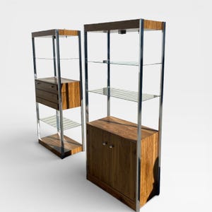 May include: Two wooden and glass display cabinets. The cabinets have a rectangular shape with a wooden frame and glass shelves. The cabinets have a wooden base and top, with a stainless steel frame. One cabinet has drawers, the other has a cabinet with doors.