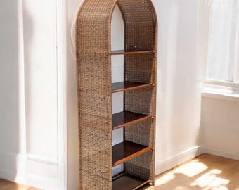 May include: A tall, arched bookshelf made of woven rattan. The natural brown shelving unit has four dark wooden shelves. The open-backed design allows light to pass through. The bookshelf is a stylish storage solution.