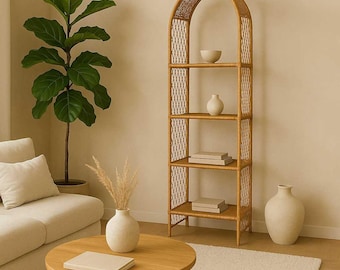 May include: A natural rattan arched bookshelf with four shelves, holding decorative items. A round wooden coffee table with a vase and a book is in front of a cream-colored sofa. A large potted plant is to the left.