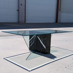 May include: A glass-top coffee table with a black and white marble base. The base is shaped like a triangle with a rectangular top. The table is sitting on a concrete surface.