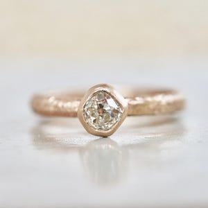 May include: A rose gold ring with a textured band and a single, round, bezel-set diamond.