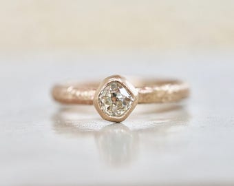 May include: A rose gold ring with a textured band and a single, round, bezel-set diamond.