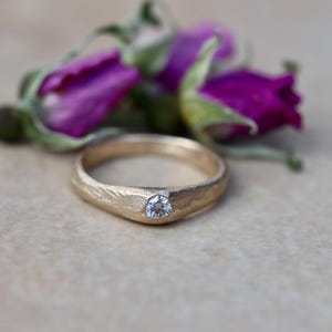 May include: A gold ring with a textured band and a single, round diamond set in the center.