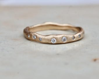 May include: A gold ring with a textured surface and a wavy design. The ring is adorned with several small, round, clear diamonds. The ring is set against a neutral background.