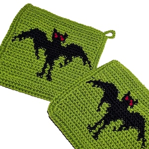 May include: Two square, lime green crocheted potholders. Each potholder features a black bat with red eyes. The potholders have a loop for hanging. Ideal for Halloween or a spooky kitchen.