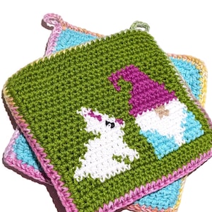 Könnte beinhalten: Zwei handgefertigte gehäkelte Topflappen. Der obere Topflappen ist grün mit einem Zwerg- und Einhorn-Design. Der Zwerg hat einen lila Hut und blaue Kleidung. Das Einhorn ist weiß. Der Topflappen hat einen rosa Rand.