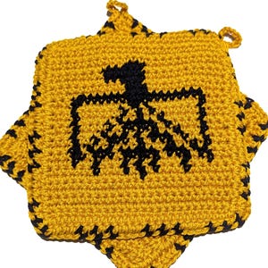 May include: Handmade crochet potholder in a starburst shape. The potholder is yellow with a black eagle design in the center. The edges are outlined in black. It has a loop for hanging. A kitchen accessory.