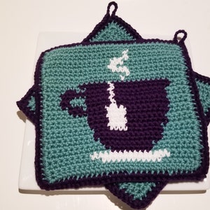 Puede incluir: Dos agarraderas de olla de color turquesa tejidas a crochet con un diseño de taza de café de color morado tejido a crochet. Las agarraderas tienen un lazo para colgar.