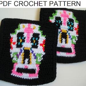 Könnte beinhalten: Zwei schwarze Häkel-Topflappen mit einem bunten Zucker Schädel Design. Die Schädel sind weiß mit rosa, grünen, gelben, blauen und violetten Akzenten.