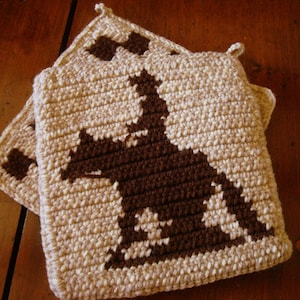 May include: Two crocheted pot holders with a brown silhouette of a horse on a beige background.