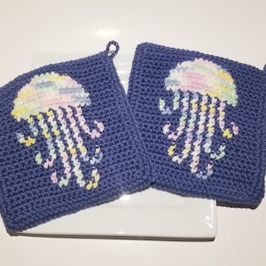 Puede incluir: Dos posavasos de ganchillo azul con un diseño de medusa colorido. Las medusas están hechas con una variedad de colores pastel.