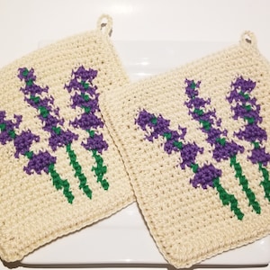 Peut inclure: Deux maniques à fleurs de lavande crochetées avec un fond blanc, des tiges vertes et des fleurs violettes.