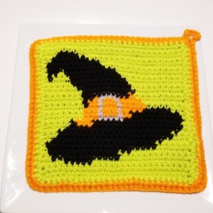 May include: A green crocheted pot holder with an orange border and a black witch hat design.