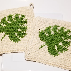 May include: Two crocheted pot holders with a green leaf design. The pot holders are square and have a cream background.
