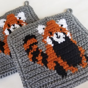 May include: Two gray crocheted pot holders with red panda designs. The red pandas are crocheted in orange, black, and white yarn.