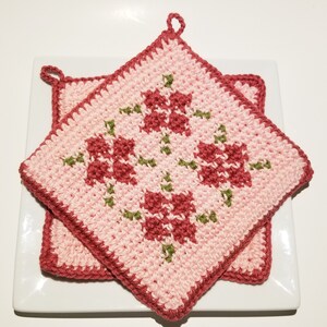 Könnte beinhalten: Zwei rosa und rote gehäkelte Topflappen mit Blumenmuster. Die Topflappen haben eine Schlaufe zum Aufhängen.