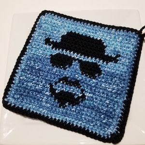 Puede incluir: Un agarrador cuadrado de ganchillo con una silueta negra estilizada de un hombre con sombrero y gafas de sol sobre un fondo azul y blanco. Tiene un borde negro y un lazo para colgar.