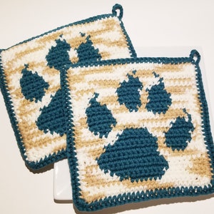 May include: Two square, crocheted potholders. Each potholder features a paw print design in teal blue, set against a background of alternating beige and white stripes. The edges are trimmed with teal blue yarn, and each has a loop for hanging.