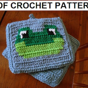 Puede incluir: Posavasos de ganchillo con forma de rana en verde, blanco y negro sobre fondo gris. El posavasos está doblado por la mitad.