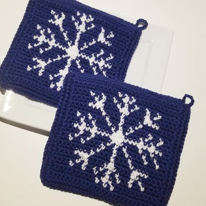 Pode incluir: Dois pegadores de panela de crochê azul com desenhos de floco de neve branco.