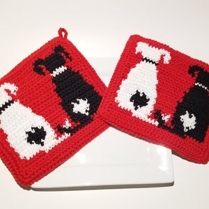 Puede incluir: Dos agarraderas de olla de crochet rojo con diseños de perros negros y blancos. Los perros están sentados de espaldas.
