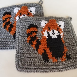 May include: Two gray crocheted pot holders with red panda designs. The red pandas are crocheted in orange, black, and white.
