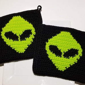 May include: Two black and green crocheted pot holders with an alien face design.