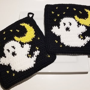 Könnte beinhalten: Zwei schwarze gehäkelte Topflappen mit einem weißen Geist und einem gelben Halbmond-Design. Die Topflappen haben einen schwarzen Hintergrund mit gelben Sternen.