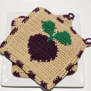 May include: Two crocheted pot holders with a purple beet and green leaves design. The pot holders have a brown border and a purple trim.