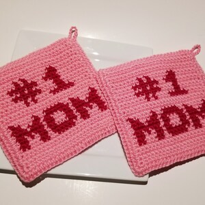May include: Two pink crocheted pot holders with the words "#1 MOM" in red.