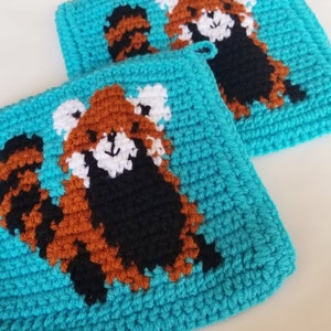 May include: Two crocheted pot holders with a red panda design on a turquoise background.
