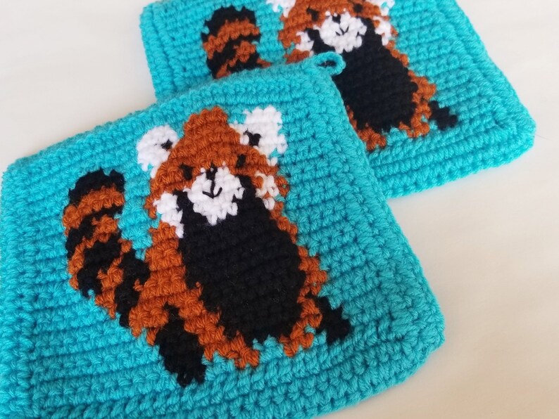 May include: Two crocheted pot holders with a red panda design on a turquoise background.