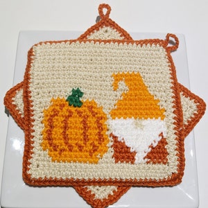 Puede incluir: Dos agarraderas de olla de ganchillo con temática otoñal. Una agarradera tiene una calabaza y la otra un gnomo.