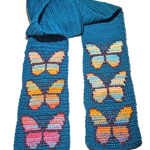 May include: A teal crochet scarf featuring six colorful butterfly appliqués. The butterflies have orange, yellow, pink, and blue wings. The scarf is made of a soft, textured yarn, perfect for adding a touch of handmade charm to any outfit.
