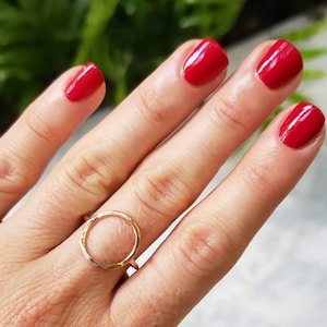 May include: A gold ring with a simple circle design. The ring is on a finger with red nail polish.