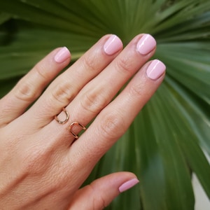 May include: A gold ring with a unique open design. The ring is worn on the middle finger of a hand with pink nail polish.