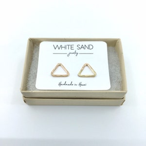 May include: A pair of gold triangle earrings in a white box with the text "WHITE SAND jewelry Handmade in Hawaii".