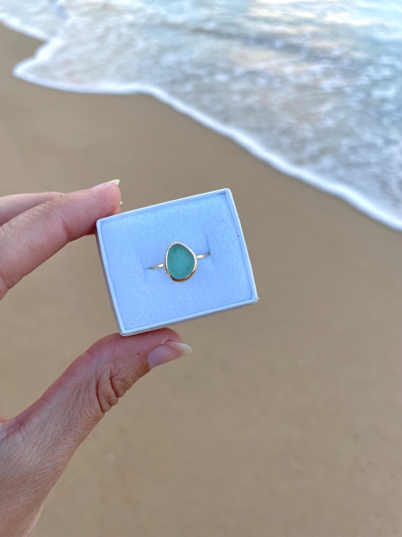 May include: A teardrop-shaped ring with a light blue gemstone set in a gold band. The ring is in a white box.