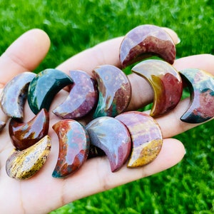 May include: A collection of polished, multi-colored, crescent moon shaped stones. The stones are a mix of red, orange, yellow, green, and brown.