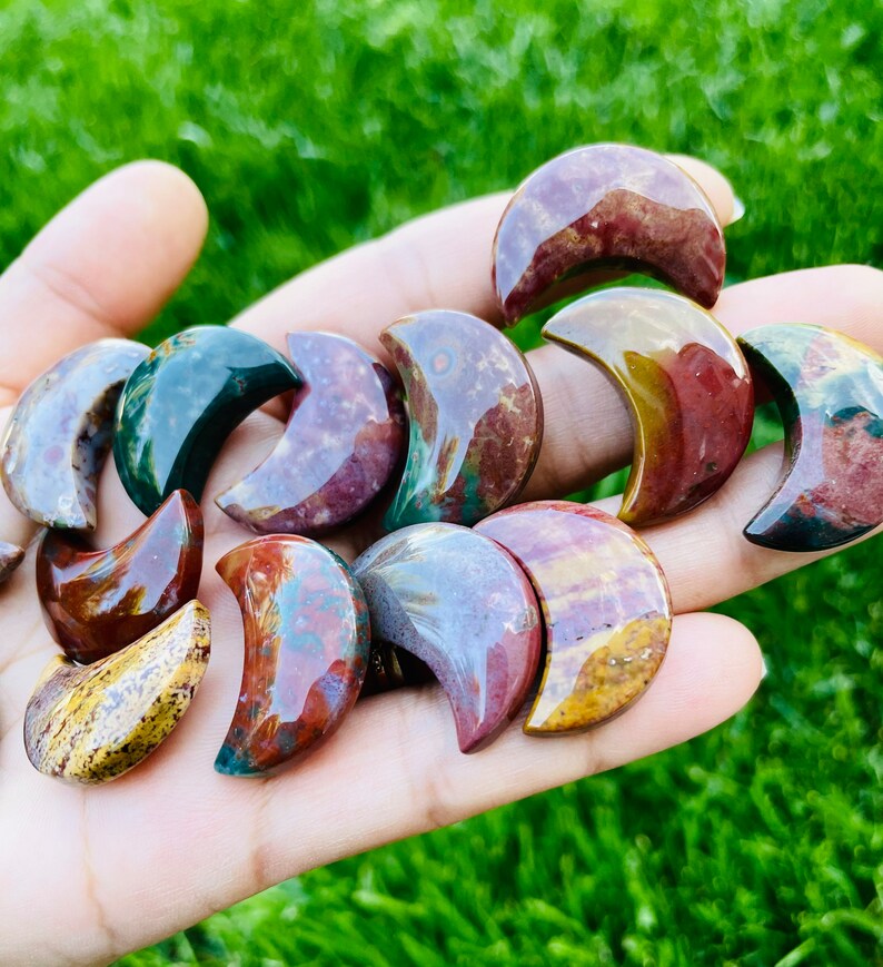 May include: A collection of polished, multi-colored, crescent moon shaped stones. The stones are a mix of red, orange, yellow, green, and brown.