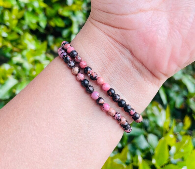 May include: A pink and black beaded bracelet with a stretchy band. The bracelet is made of small, round beads that are a mix of pink and black.